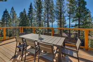 Eine Holzterrasse mit Tisch und Stühlen mit Blick auf einen Wald und ein Gewässer.