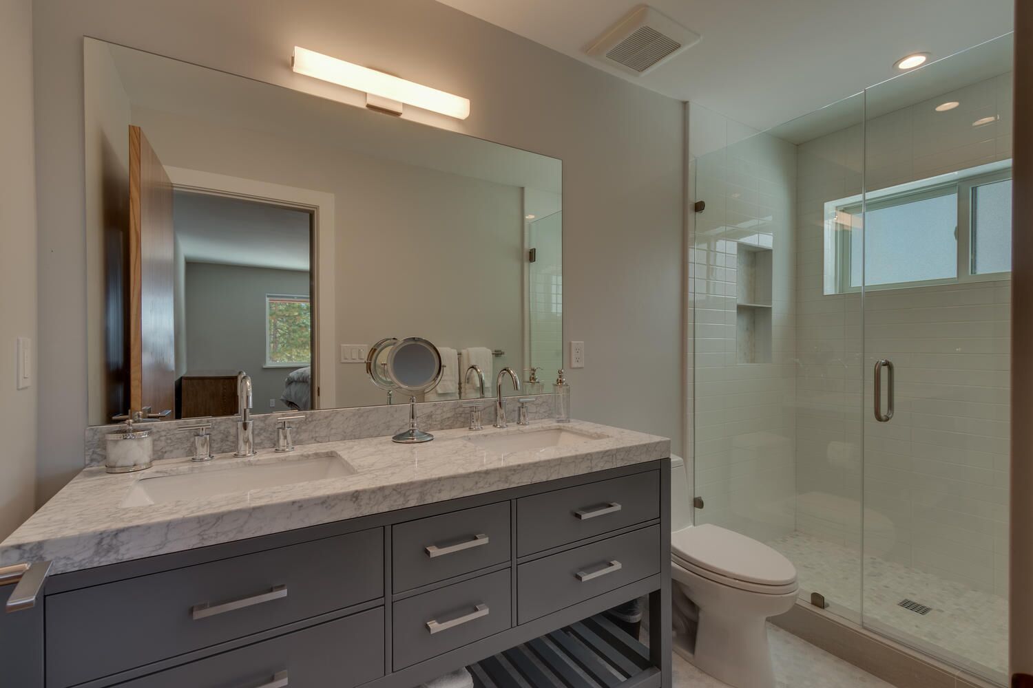 A modern bathroom with a marble vanity, a large mirror, a glass shower enclosure, and a toilet.