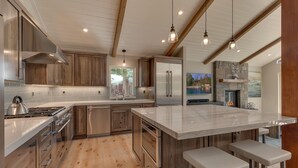 A modern kitchen with a large island, stainless steel appliances, wooden cabinets, and pendant lighting.