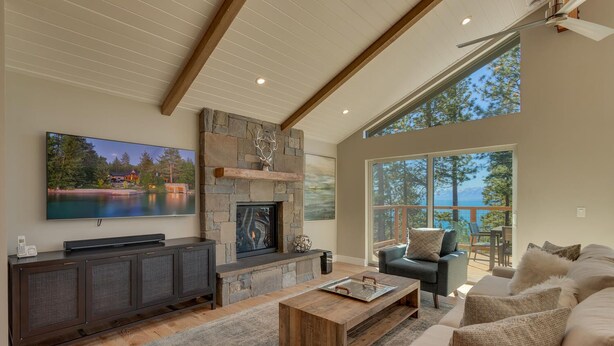 A spacious living room with a stone fireplace, a large flat-screen TV, and a comfortable seating area with a view of the outdoors.