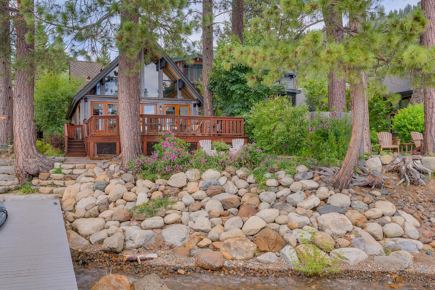 Une cabane dotée d’une terrasse en bois, entourée de gros rochers et d’arbres.