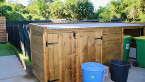 Een houten tuinhuis met een golfplaten dak, een blauwe waterbak en twee groene vuilnisbakken.