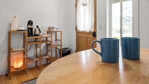 Une table en bois avec deux tasses bleues, une étagère en bois avec des livres et une bouilloire, et une lampe allumée.