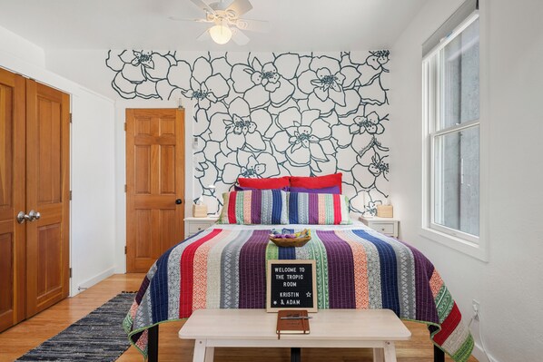 A bedroom with a bed, a nightstand, a wooden door, a window, and a wall with a floral pattern. - The Tropic Room at River Stone Inn at Bryce (Tropic)