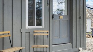 Une maison grise avec une porte grise, une fenêtre et un banc à l’extérieur.