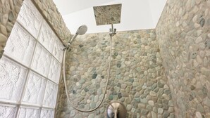 Une douche avec un mur en pierre, une porte en verre et un pommeau de douche.
