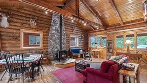 A log cabin interior with a stone fireplace, wooden furniture, and a cozy seating area.