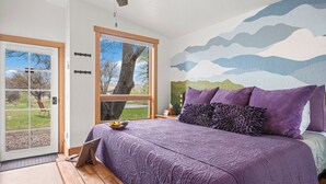 A bedroom with a large bed, a view of the outdoors through a sliding door, and a mural on the wall. - The Walnut Tree Room at River Stone Inn at Bryce (Tropic)