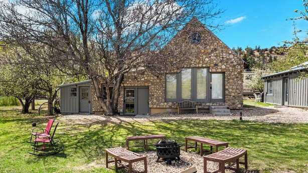 A stone house with a chimney, a fire pit, and wooden furniture in a grassy yard. - The Walnut Tree Room at River Stone Inn at Bryce (Tropic)
