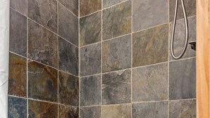 A shower with a stone tile wall and a pebble-patterned floor. - The Walnut Tree Room at River Stone Inn at Bryce (Tropic)