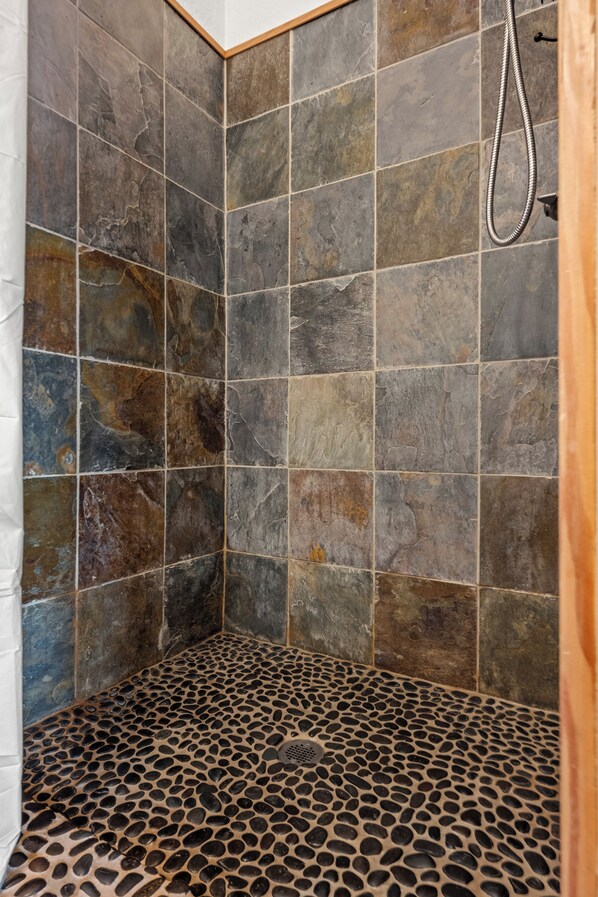 A shower with a stone tile wall and a pebble-patterned floor.
