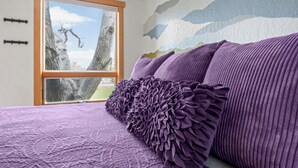A bedroom with a large window, a purple bedspread, and a mountain mural on the wall. - The Walnut Tree Room at River Stone Inn at Bryce (Tropic)
