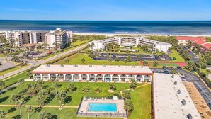 An aerial view of a resort with a swimming pool, multiple buildings, and a beach.