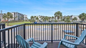 A balcony with two chairs, a view of a parking lot, and buildings in the background.