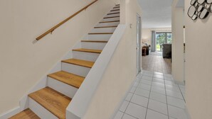 A staircase with wooden steps and white walls, leading to a room with a view of the outdoors.