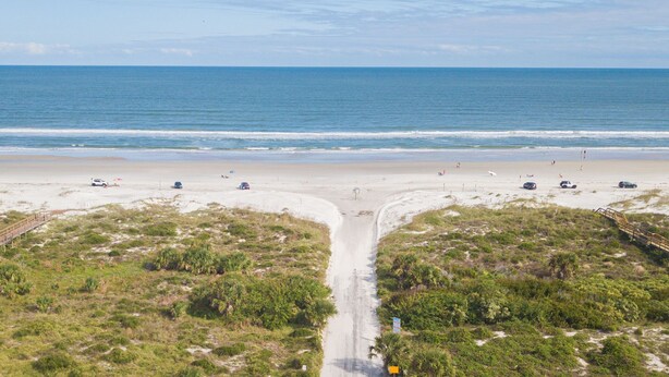 A beach with a sandy path leading to the ocean, surrounded by vegetation.