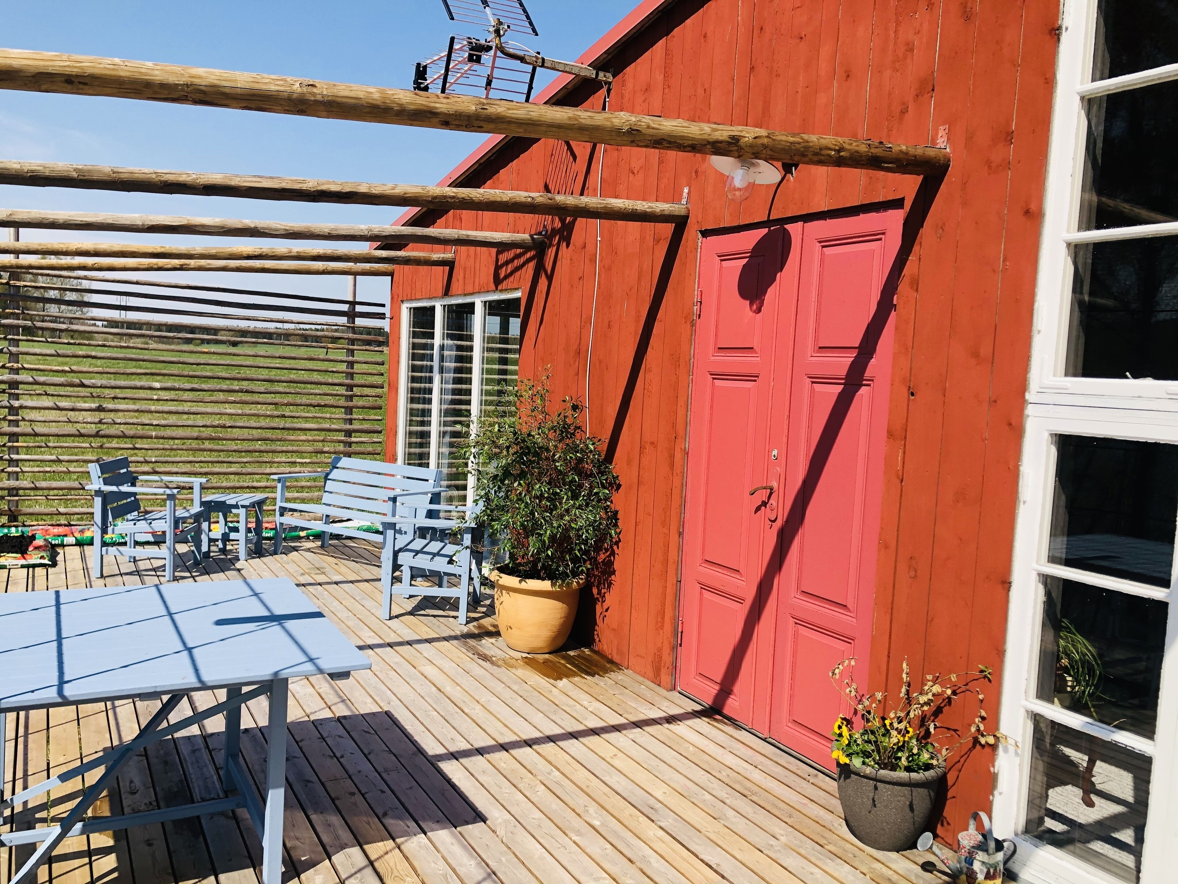 A red building with a wooden deck, a table, chairs, and potted plants.