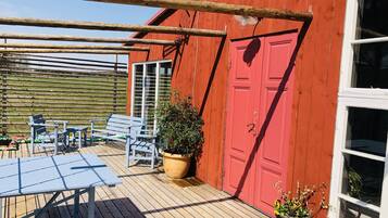 A red building with a wooden deck, a table, chairs, and potted plants.