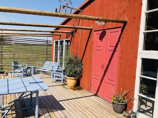 A red building with a wooden deck, a table, chairs, and potted plants. - Liljekonvalj Cottage Overlooking the River Sauna (Avesta)