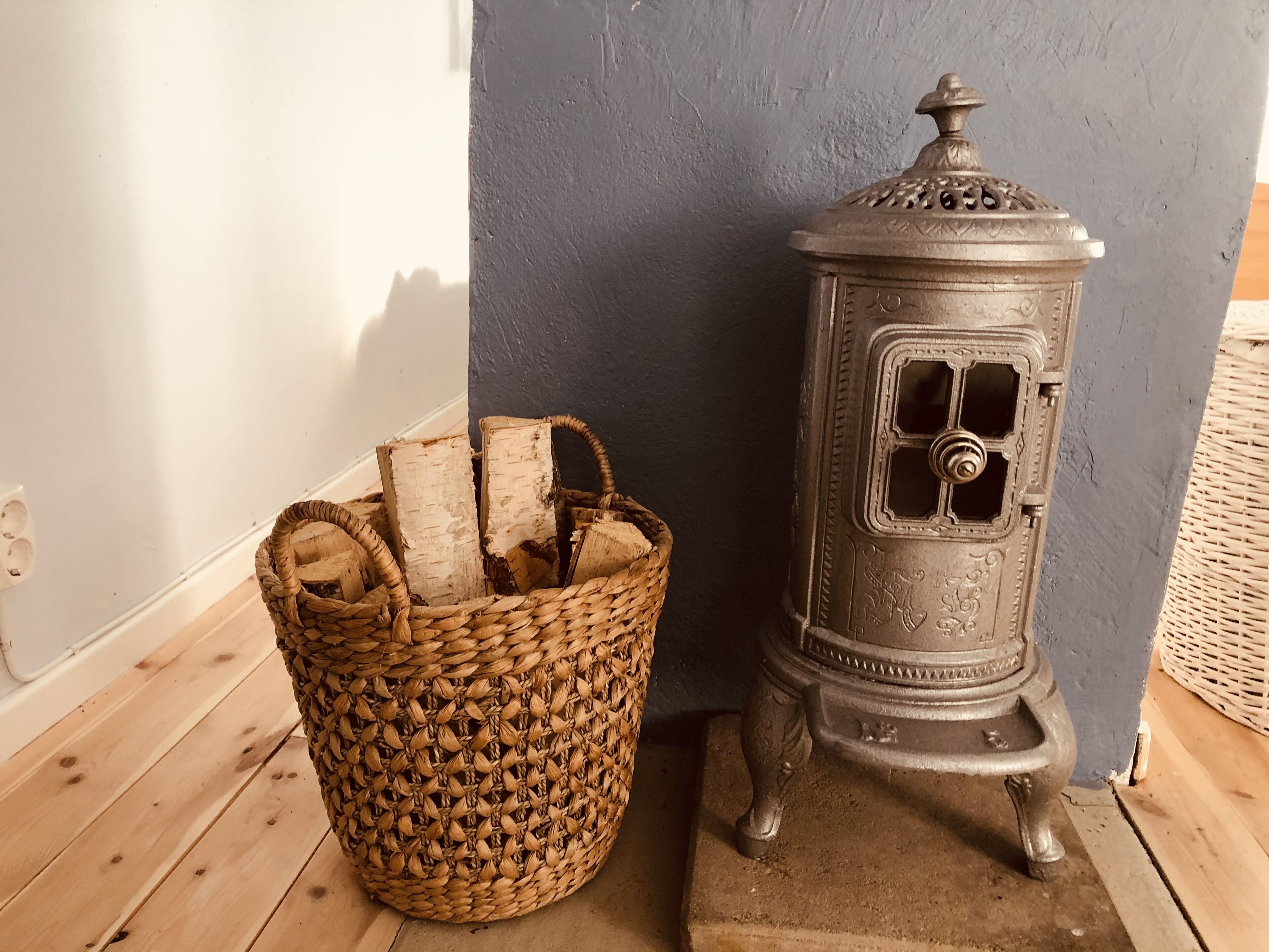 A woven basket filled with firewood next to a metal stove.