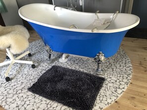 A blue freestanding bathtub with a white basin, a small white towel, and a black bath mat on a pebble-patterned floor. - Liljekonvalj Cottage Overlooking the River Sauna (Avesta)