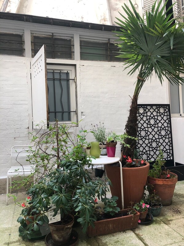 A small patio area with various potted plants, a white metal table, and a white chair.
