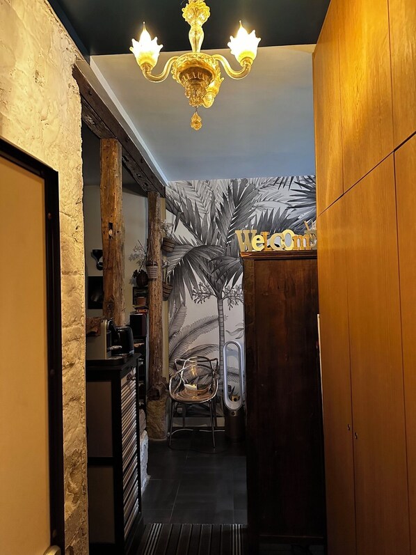 A narrow hallway with a wooden door, a black-framed mirror, and a wall with a palm tree mural. - 2-room apartment that feels like a house (Paris)