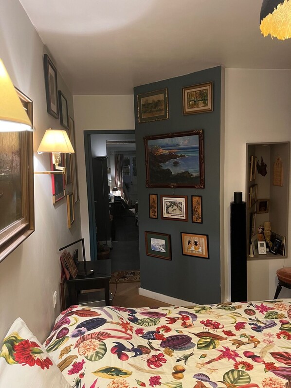 A bedroom with a floral bedspread, framed artwork on the walls, and a lamp by the bed.