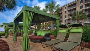 Een overdekt terras met groene luifels, comfortabele lounge fauteuils en een rieten bank.