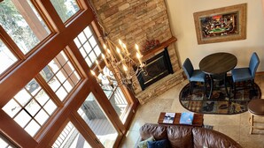 A cozy living room with a fireplace, a leather sofa, a dining table with chairs, and large windows. - Ski-in Ski-out, Mountain View, Luxury Townhome, Purgatory Resort (Durango)