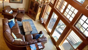 A spacious living room with a brown leather sofa, a wooden coffee table, and a chandelier. There is a large window with a view of the outside. - Ski-in Ski-out, Mountain View, Luxury Townhome, Purgatory Resort (Durango)