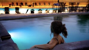 A poolside view with a person leaning on the edge, overlooking a pool and lounge area with chairs and tables. - Ski-in Ski-out, Mountain View, Luxury Townhome, Purgatory Resort (Durango)