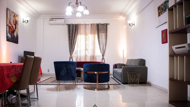 Een moderne woonkamer met een eethoek, met een kroonluchter, airconditioning en een groot raam met patroon gordijnen.