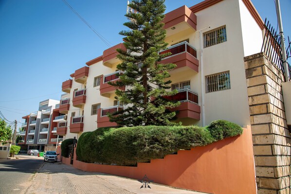 A multi-story residential building with balconies, a pine tree, and a brick wall. - Premier Residence at the heart of Dakar (Dakar)