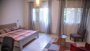 Een slaapkamer met een bed, een stoel, een klein tafeltje en een raam met gordijnen.