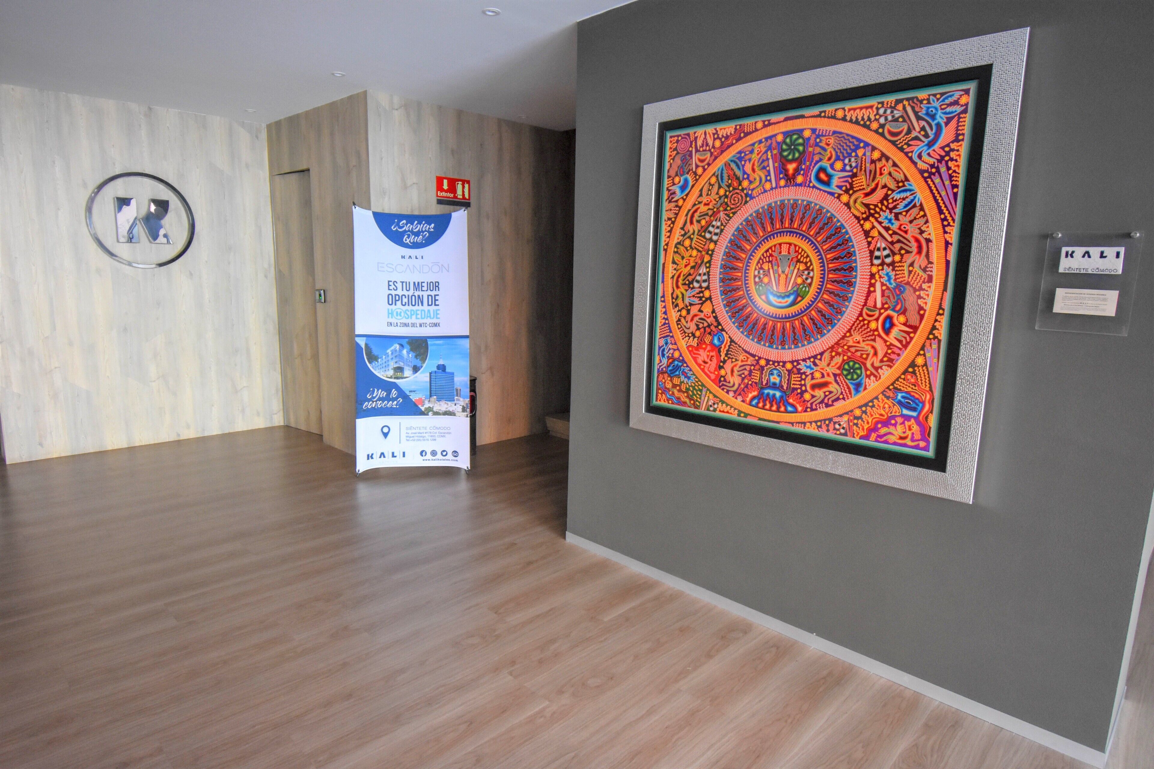 A room with a wooden floor, a framed colorful artwork on the wall, and a sign with text and logos.