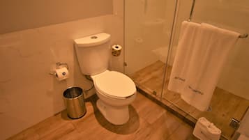 Un baño moderno con inodoro, cabina de ducha de vidrio y toallero con una toalla blanca.