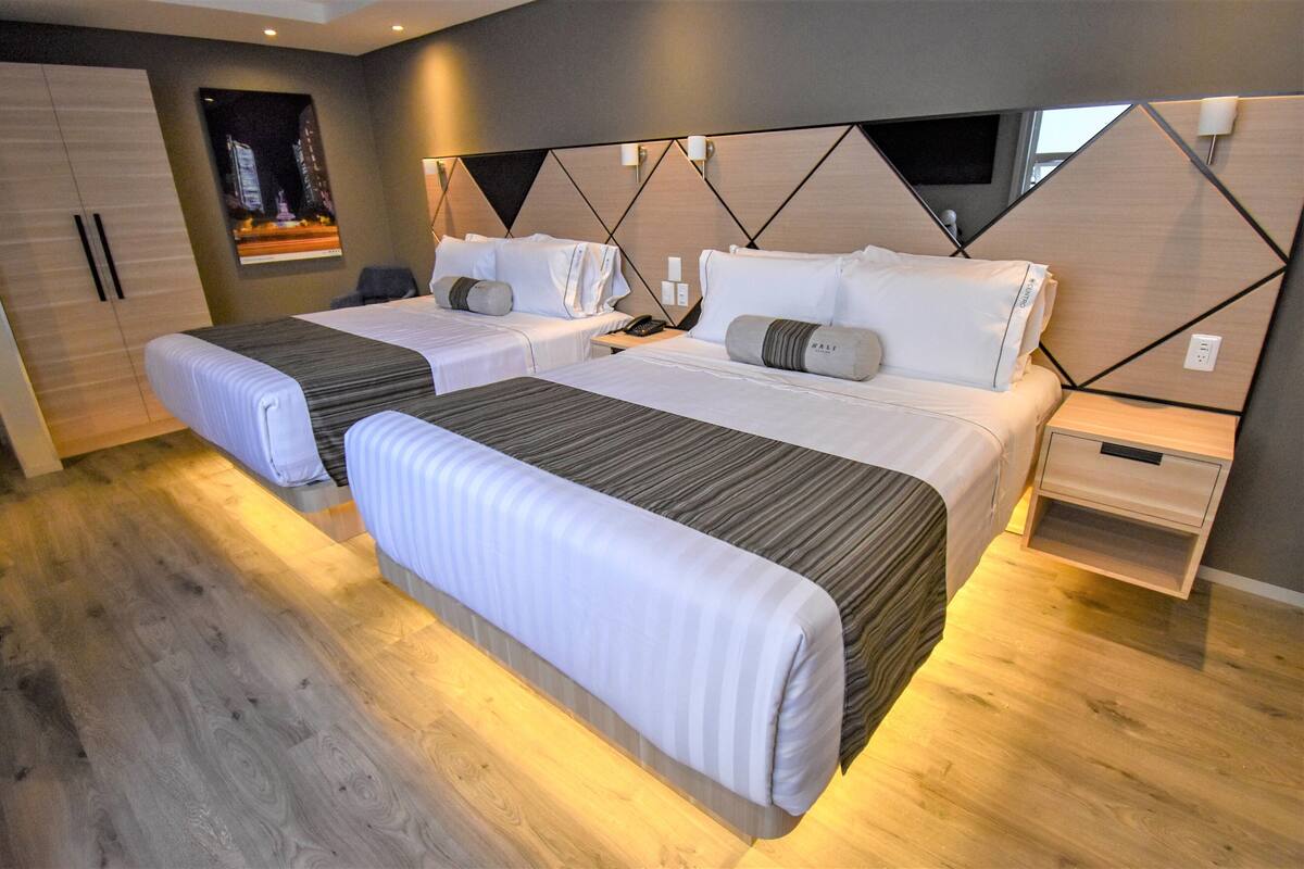 Ein Hotelzimmer mit zwei Betten, Holzboden, modernem Kopfteil und Nachttisch mit Lampe.