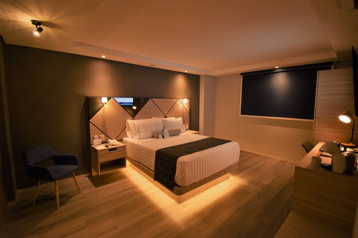 Ein modernes Hotelzimmer mit einem großen Bett, Nachttischen, einem Schreibtisch und einem Fernseher.