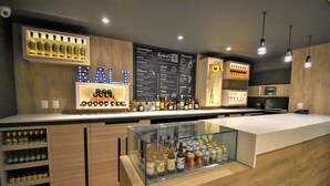 Eine Barbereich mit Holztresen, Regalen mit Flaschen, einer Kreidetafel mit der Speisekarte und hängenden Lampen.