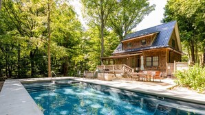 Une cabane en bois avec une piscine, entourée d’arbres.
