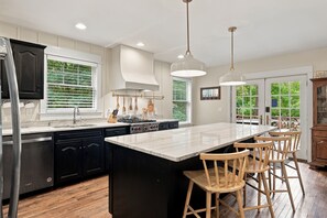 A modern kitchen with a large island, dark cabinetry, and a view of the outdoors. - (2027 OPEN!) Lake View Home with Private Pool and Hot Tub! (Harbert)