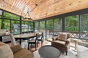 A spacious room with a large dining table, comfortable seating, and a view of a wooded area through large windows. - (2027 OPEN!) Lake View Home with Private Pool and Hot Tub! (Harbert)