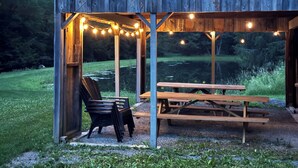 Un pabellón rústico de madera con luces de cuerda, una mesa de picnic y una silla.