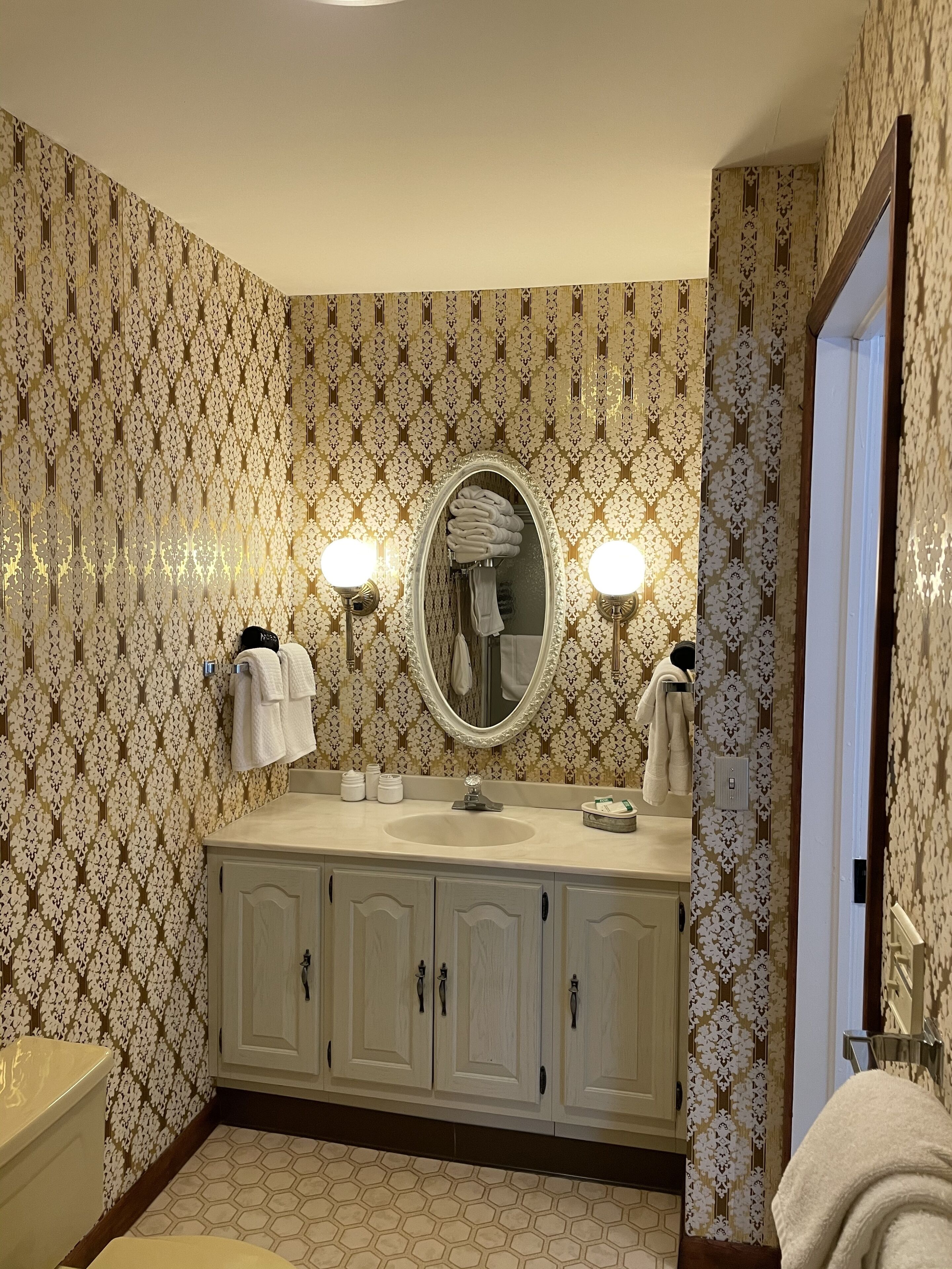Un bagno con carta da parati decorata, un mobile bagno con doppio lavabo, uno specchio e due luci a parete.