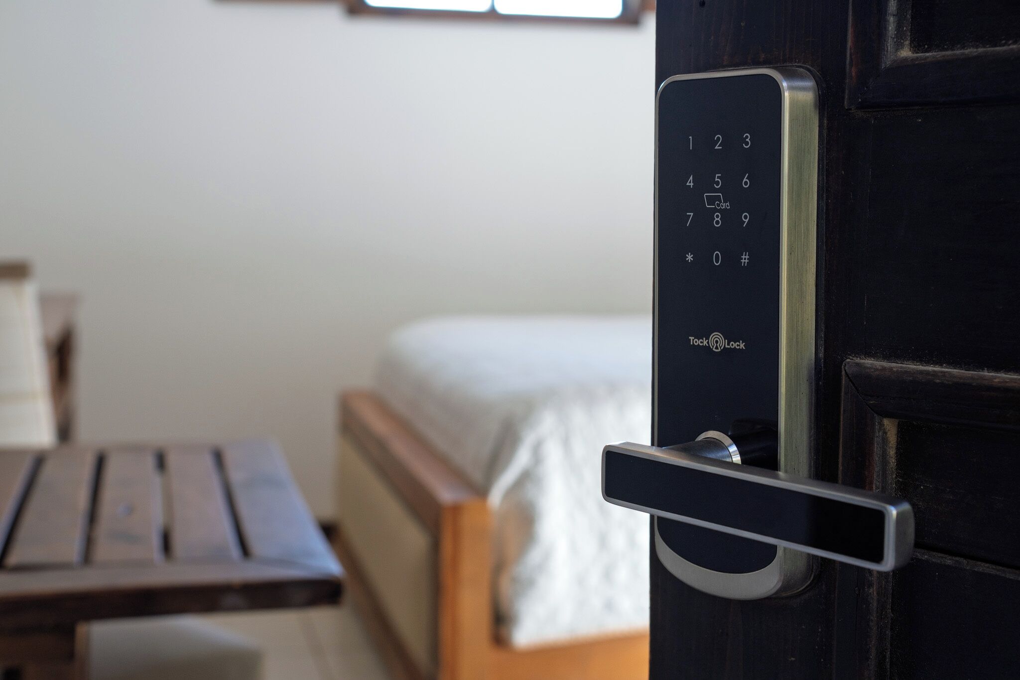 Una habitación con una cama, una mesa de madera y una puerta con teclado numérico.