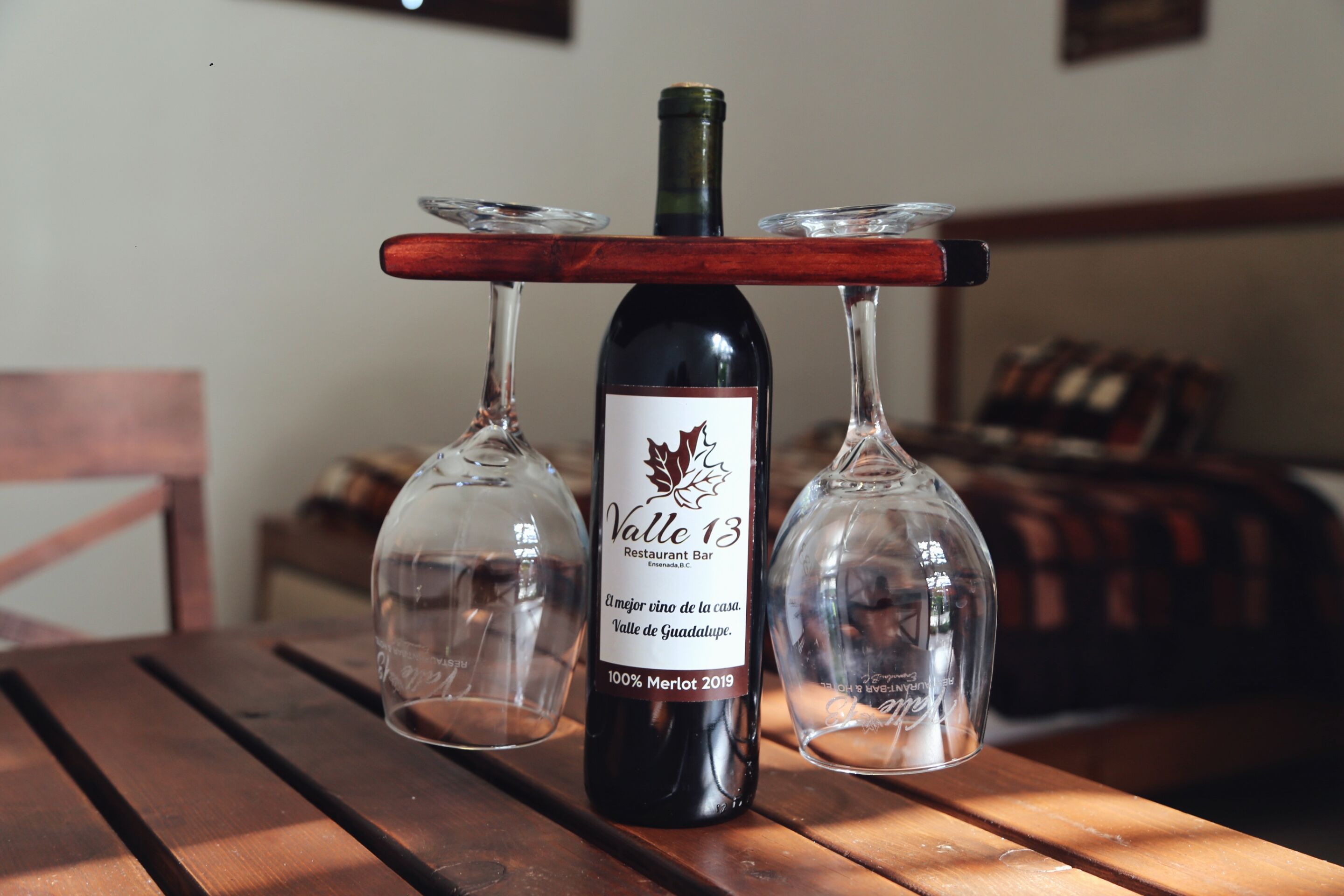 A bottle of wine on a wooden table with two empty wine glasses.