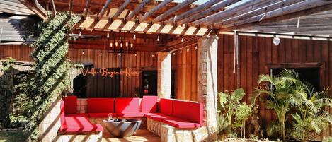 Un área de estar al aire libre con techo, cojines rojos y una chimenea.