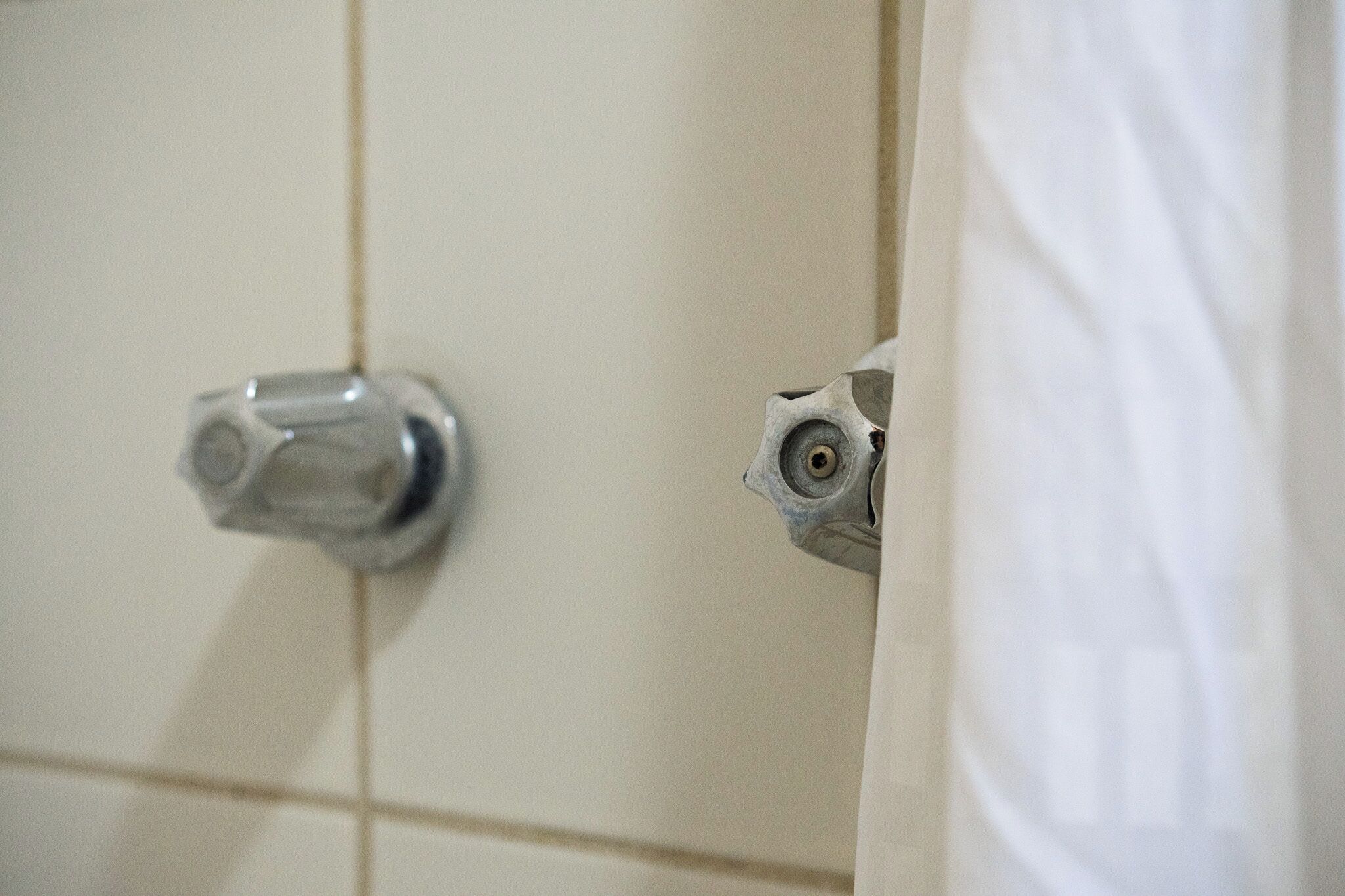 A bathroom with a white tiled wall, a silver faucet, and a partially visible white shower curtain.