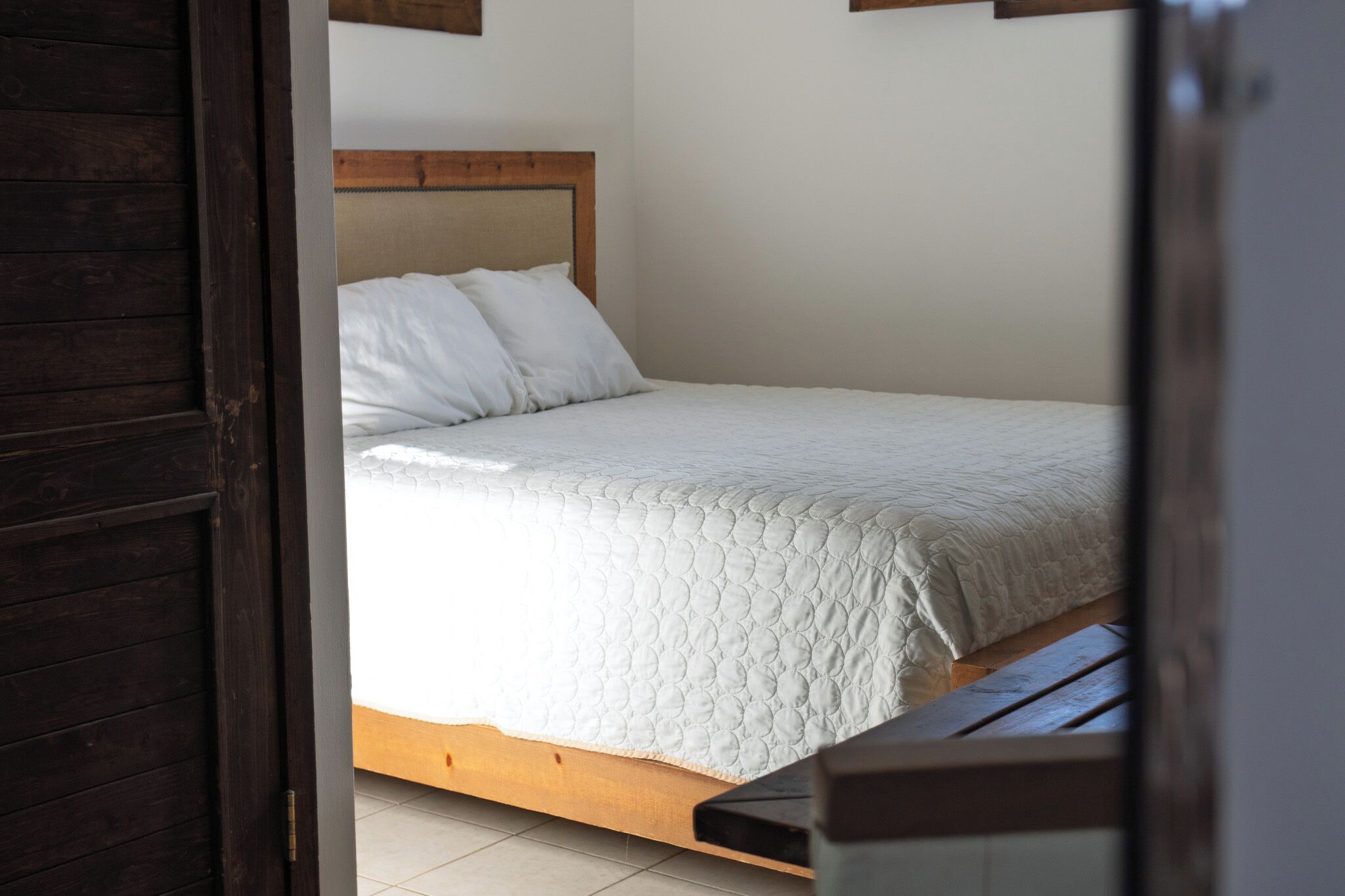 Un dormitorio con cabecera de madera, edredón blanco y un banco de madera al pie de la cama.